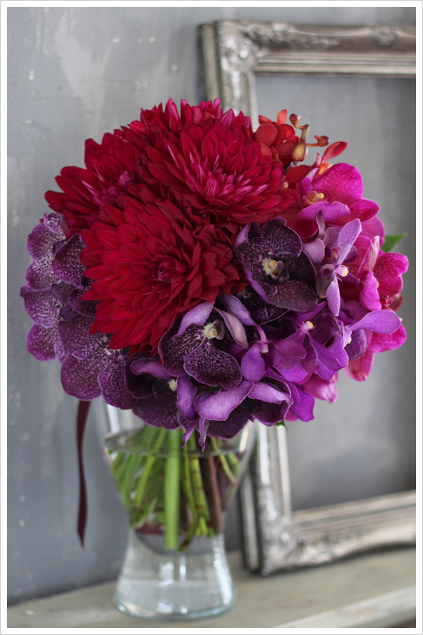 赤いダリアと紫、ワイン、ピンク系の蘭を使った大人っぽいクラッチブーケ。 花材を種類ごとにまとめて入れるグルーピングの手法でモダンでスタイリッシュに。